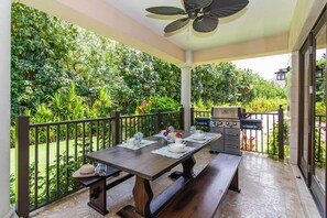 Eine überdachte Terrasse mit Esstisch für vier Personen, einem Grill und Blick auf üppiges Grün.