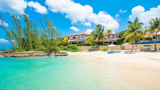 A beachfront property with a pool, palm trees, and a clear blue sky. - Casa Luna 4: Gated Luxury Near 7Mile Beach w/Pool, Heated Spa, and Private Beach Cove (Grand Cayman)