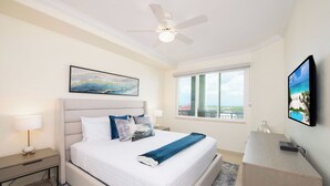 Ein Schlafzimmer mit Bett, Nachttisch, Schreibtisch, Stuhl, Deckenventilator, Fenster mit Aussicht und einem Bild an der Wand.