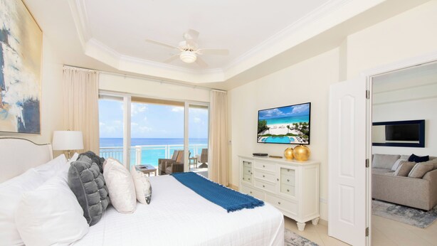 Ein Hotelzimmer mit einem Bett, einem Fernseher, einem Balkon mit Meerblick und einem Deckenventilator.