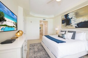 Ein Hotelzimmer mit einem großen Bett, einem Fernseher auf einer weißen Kommode, einem Bild an der Wand und Blick auf den Strand.