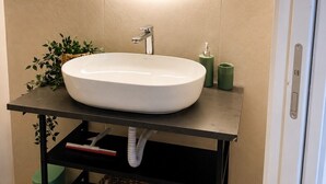 Ein Badezimmer mit rundem Spiegel, Waschbecken in Weiß, schwarzem Waschtisch und einer grünen Mülltonne.