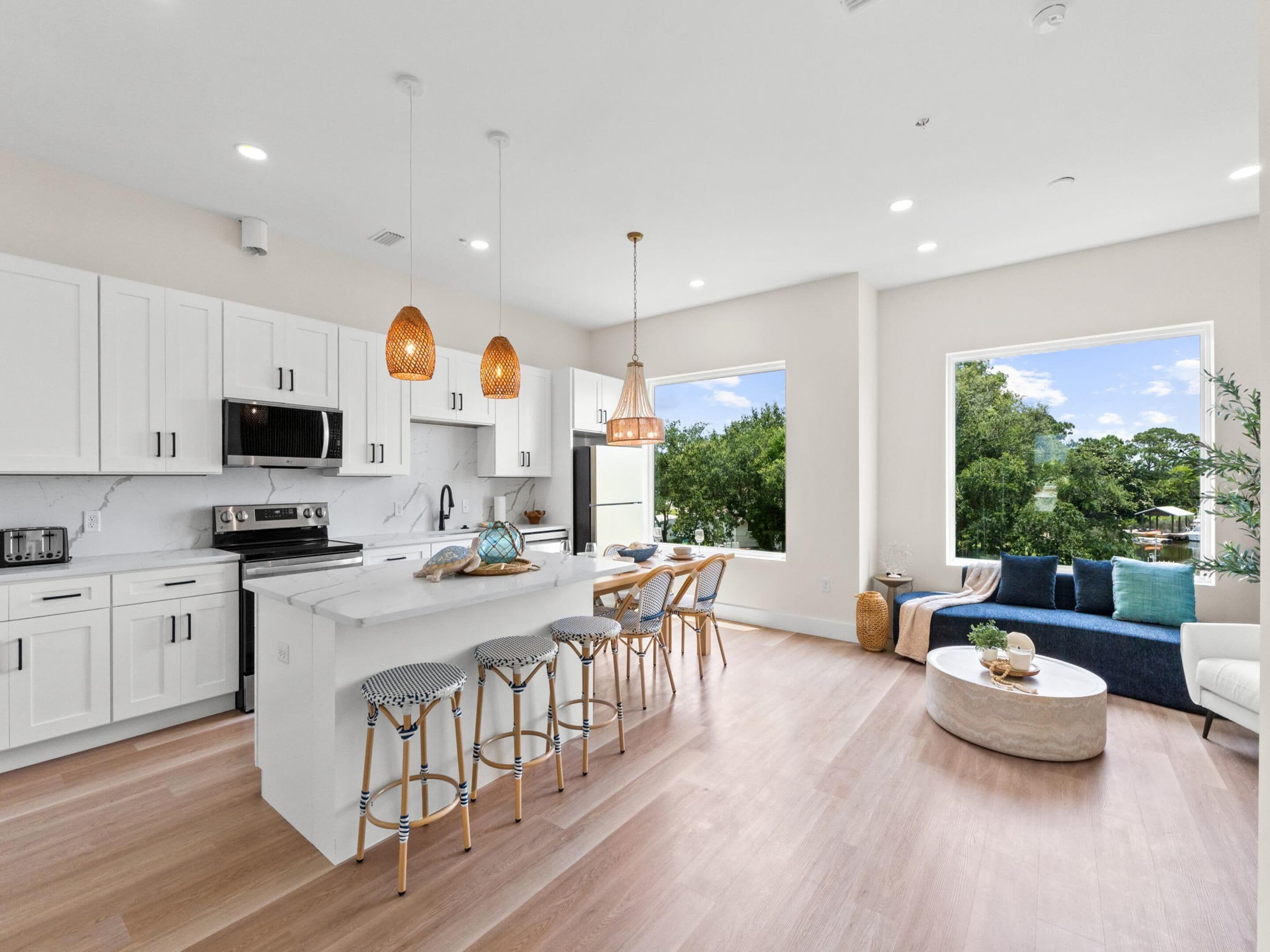 A modern kitchen with white cabinets, a central island, and bar stools. There is a dining area with a blue sofa and a round coffee table.
