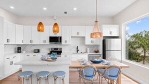 Una cucina moderna con mobili bianchi, un'isola centrale con sgabelli da bar e illuminazione a sospensione.