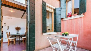 An open door leading to a dining area with a table and chairs, a window with shutters, and a small balcony with plants. - Secret Loft (Venezia)
