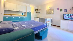Een kleine kamer met een bed, een kitchenette, een eethoek en een televisie.