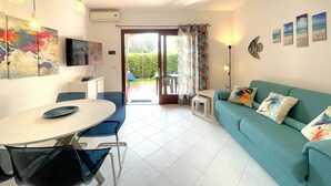 Een woonkamer met een bank, een eettafel met stoelen, een aan de muur bevestigde televisie en uitzicht door de glazen deur.