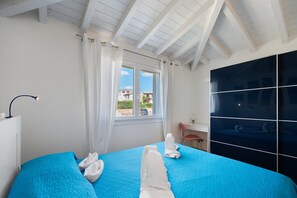 Ein Hotelzimmer mit einem großen Bett, einem Schreibtisch, einem Sessel und einem Fenster mit Vorhängen, mit Blick auf umliegende Gebäude.