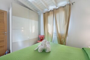 A bedroom with a green bedspread, a plush toy on the bed, a pink chair, and a sliding glass door. - Holiday Home 'R House Puntocasabudoni Budoni Cove' with Private Terrace, Wi-Fi & AC (Budoni)