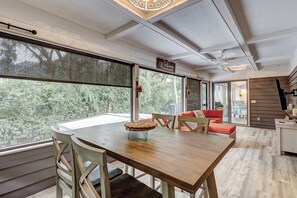 Une pièce spacieuse avec une table à manger en bois, des chaises et un canapé rouge. Une grande fenêtre offre une vue sur la verdure environnante.