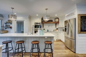 Una cucina moderna con isola centrale, sgabelli da bar, elettrodomestici in acciaio inossidabile, luci a sospensione e un orologio a parete.