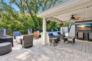 An outdoor patio area with seating, a pool, and a pergola with string lights. - 28 Ruddy Turnstone - Coastal Retreat Near the Beach with Private Pool (Hilton Head Island)