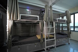 Habitació amb lliteres, un ventilador, cortines i una finestra.