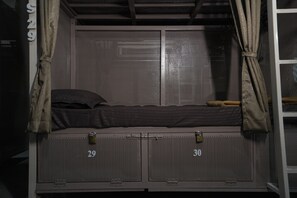 A bunk bed with a metal frame, two storage lockers below, and a window with a metal grill.