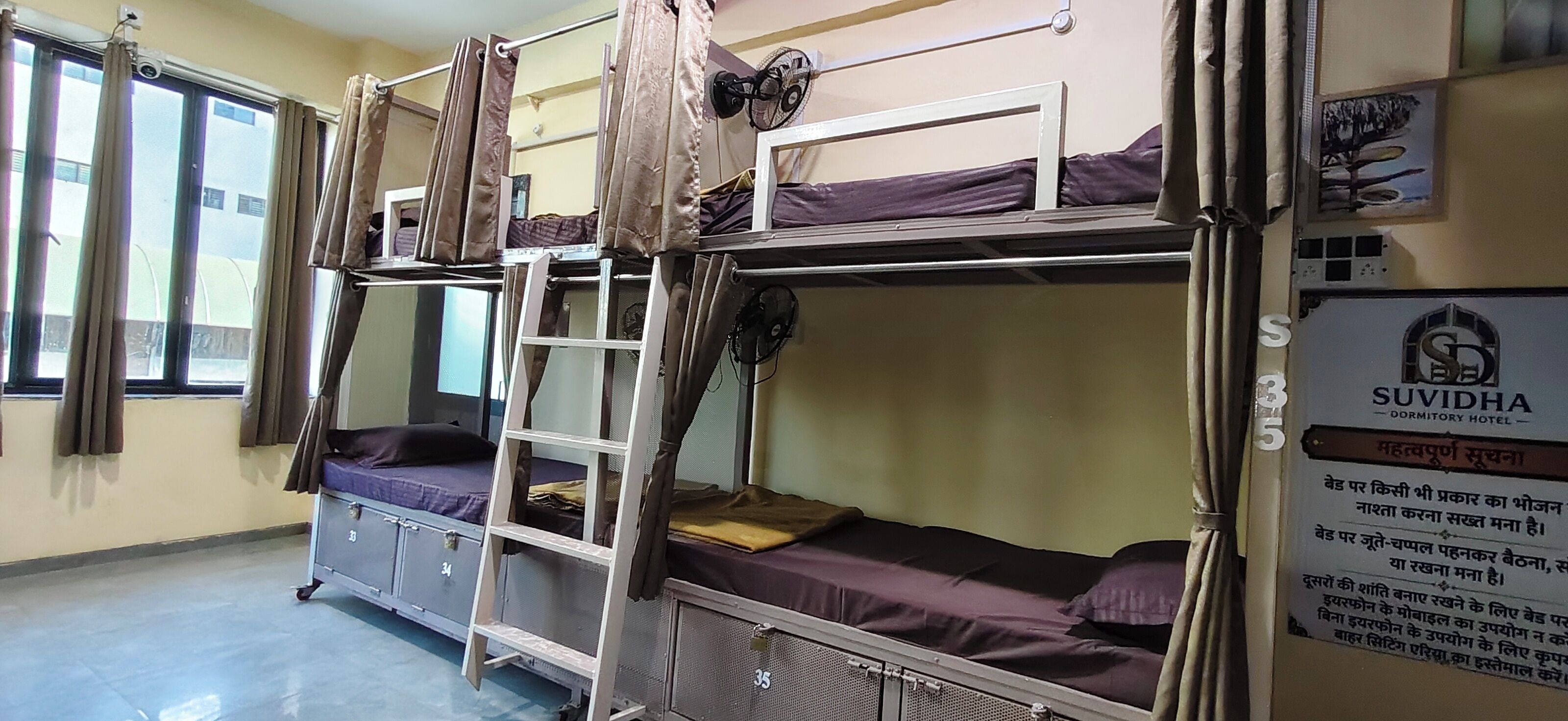 A dormitory room with bunk beds, a ladder, and a sign indicating it's part of the SUDIDHA DORMITORY HOTEL.