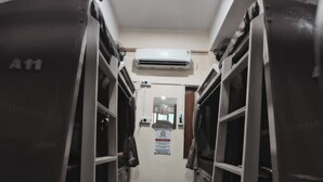 Un pasillo estrecho con taquilleras metálicas a ambos lados, una unidad de aire acondicionado en lo alto y una puerta al final.