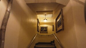 Una escalera con barandilla, una lámpara y cuadros en las paredes.