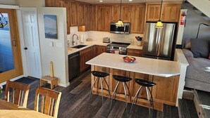 Een moderne keuken met houten kastjes, een centraal eiland met barkrukken, een magnetron, fornuis en koelkast.