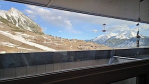 Uitzicht vanuit een raam op een berglandschap, met besneeuwde toppen en een stad daaronder.