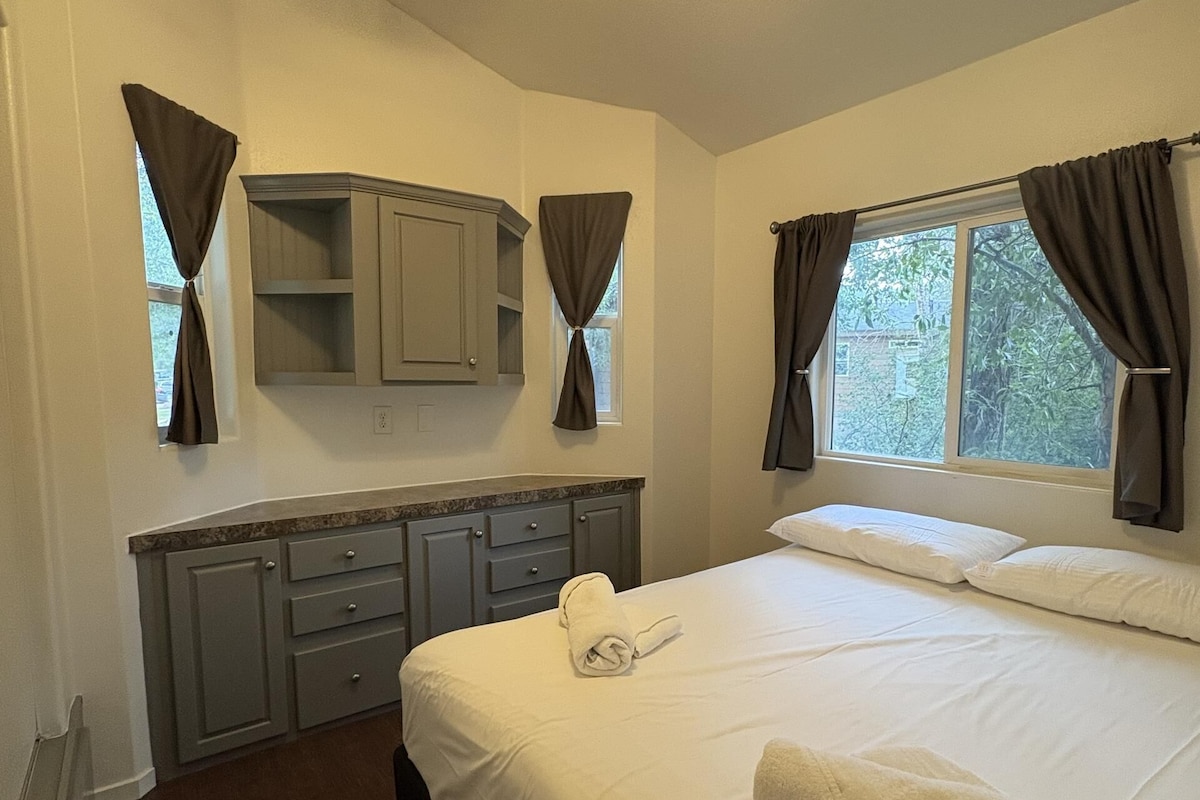A bedroom with a bed, a ceiling fan, a window with curtains, a built-in cabinet, and a radiator.