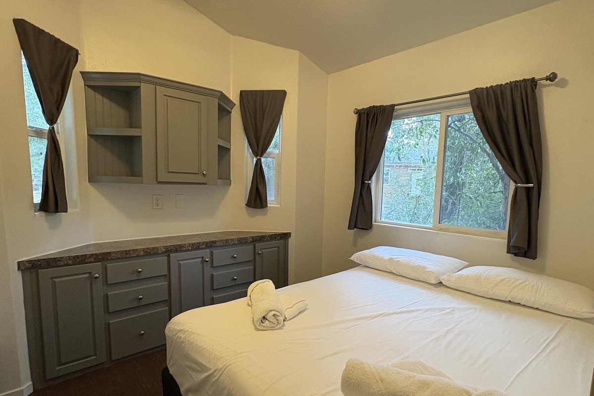 A bedroom with a bed, a ceiling fan, a window with curtains, and a built-in cabinet.