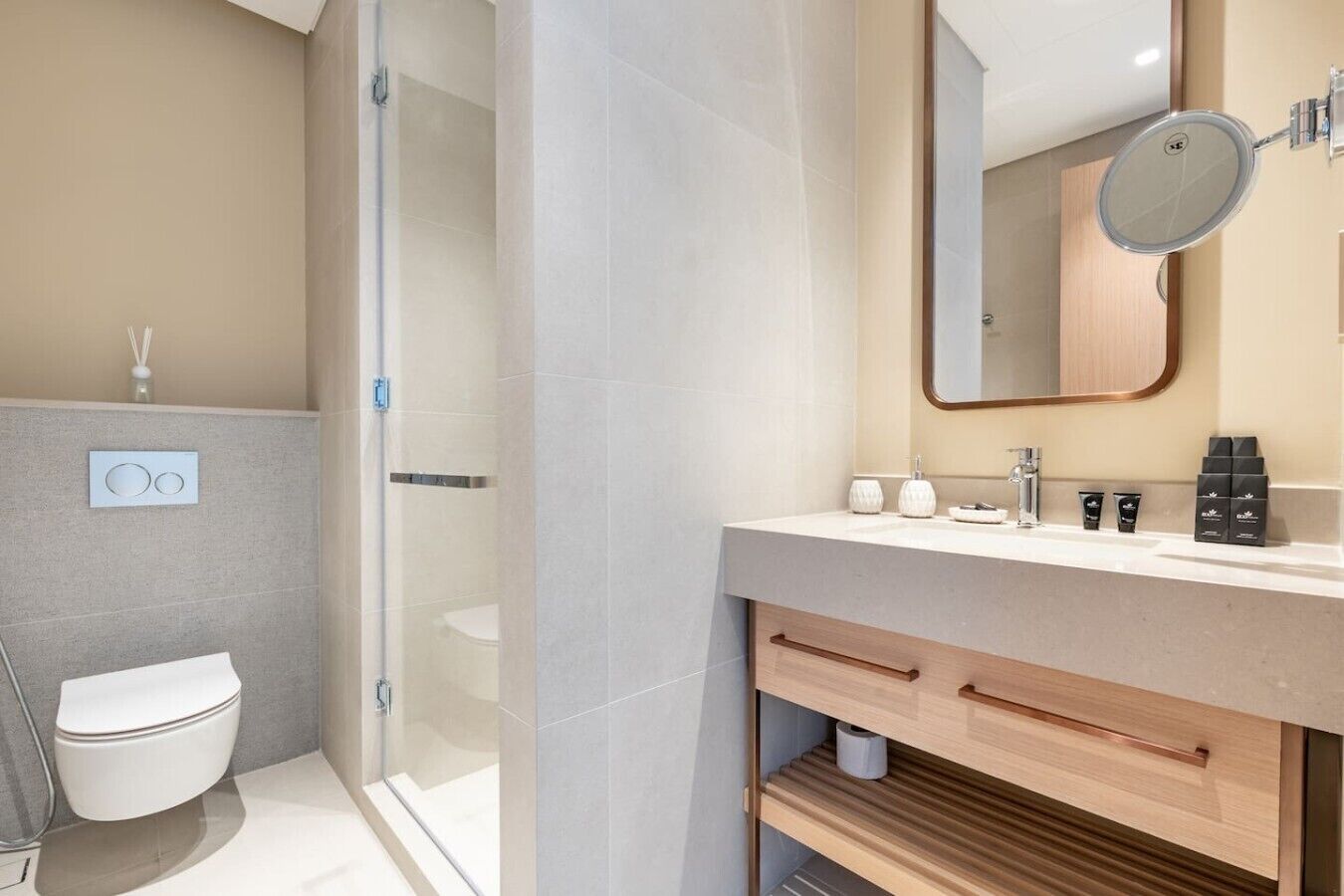 Une salle de bain moderne avec une douche à parois de verre, des toilettes, un lavabo avec des articles de toilette et un miroir.
