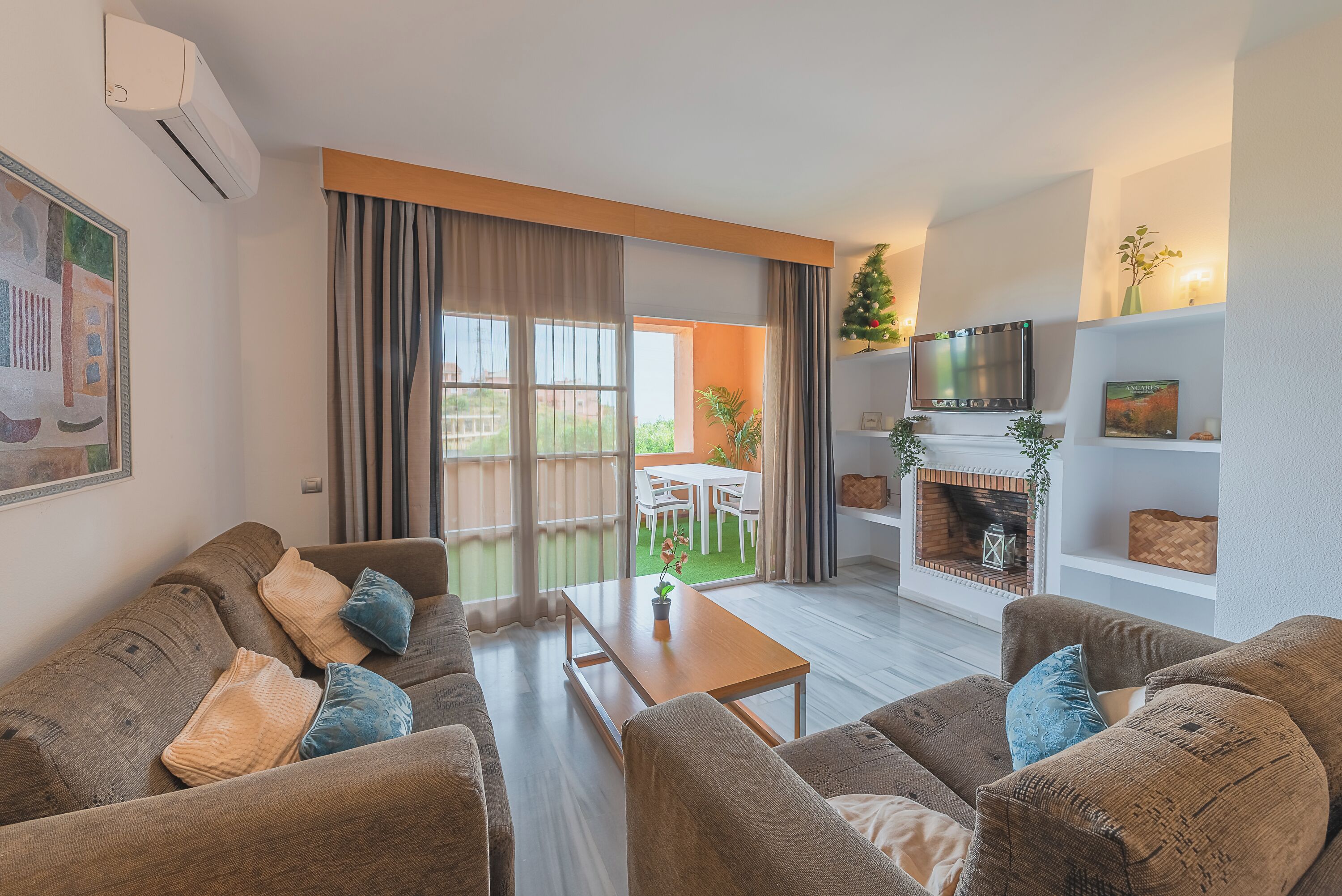 Een woonkamer met een zithoek, een salontafel, een open haard, een televisie, en een eetgedeelte zichtbaar door een glazen deur.
