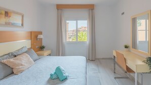 Habitación de hotel con cama, mesita de noche, lámpara, ventana con cortinas y escritorio con espejo.