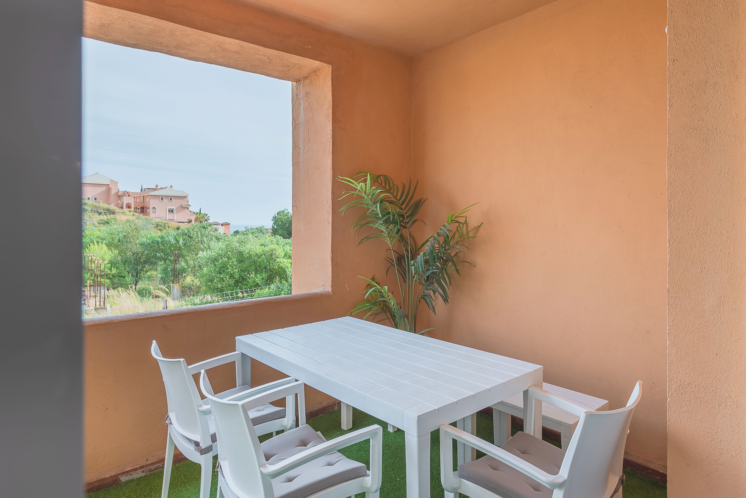 Un balcone con tavolo e sedie bianche, una pianta in vaso e vista sui palazzi.