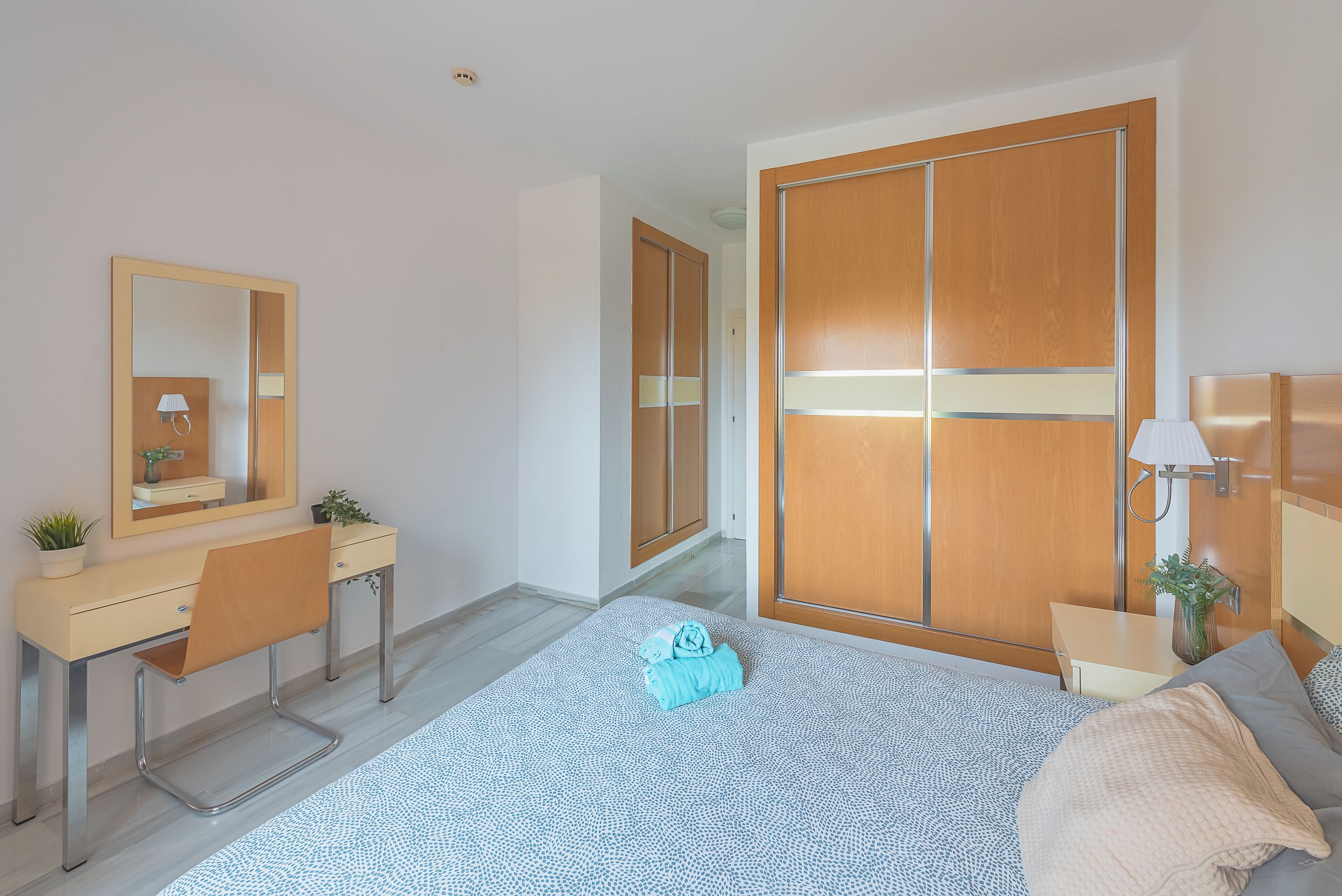 Een moderne slaapkamer met een bed, een bureau, een stoel, een kledingkast en een spiegel.