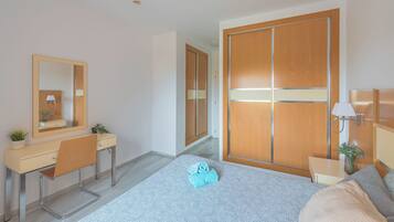 Een moderne slaapkamer met een bed, een bureau, een stoel, een kledingkast en een spiegel.