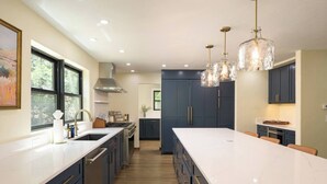 Een moderne keuken met een groot eiland, donkere kastjes en hanglampen.
