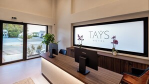 Un mostrador de recepción de hotel con dos monitores Lenovo, una barra de recepción y un amplio ventanal con vista a la calle.