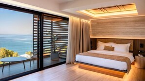 Un dormitorio moderno con una cama grande, vistas al mar y un balcón con mesa y sillas.