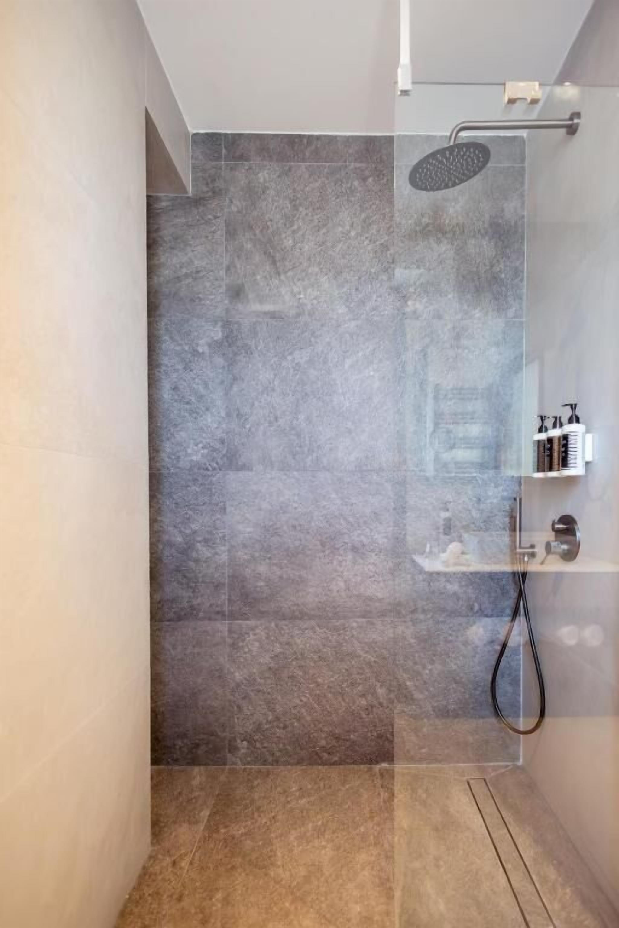 A shower with a handheld showerhead, a glass enclosure, and a shelf with toiletries.