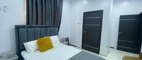 A hotel room with a bed, a nightstand, a chair, and two doors.