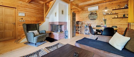A cozy cabin interior with a fireplace, wooden walls, a dining area, and a sofa.