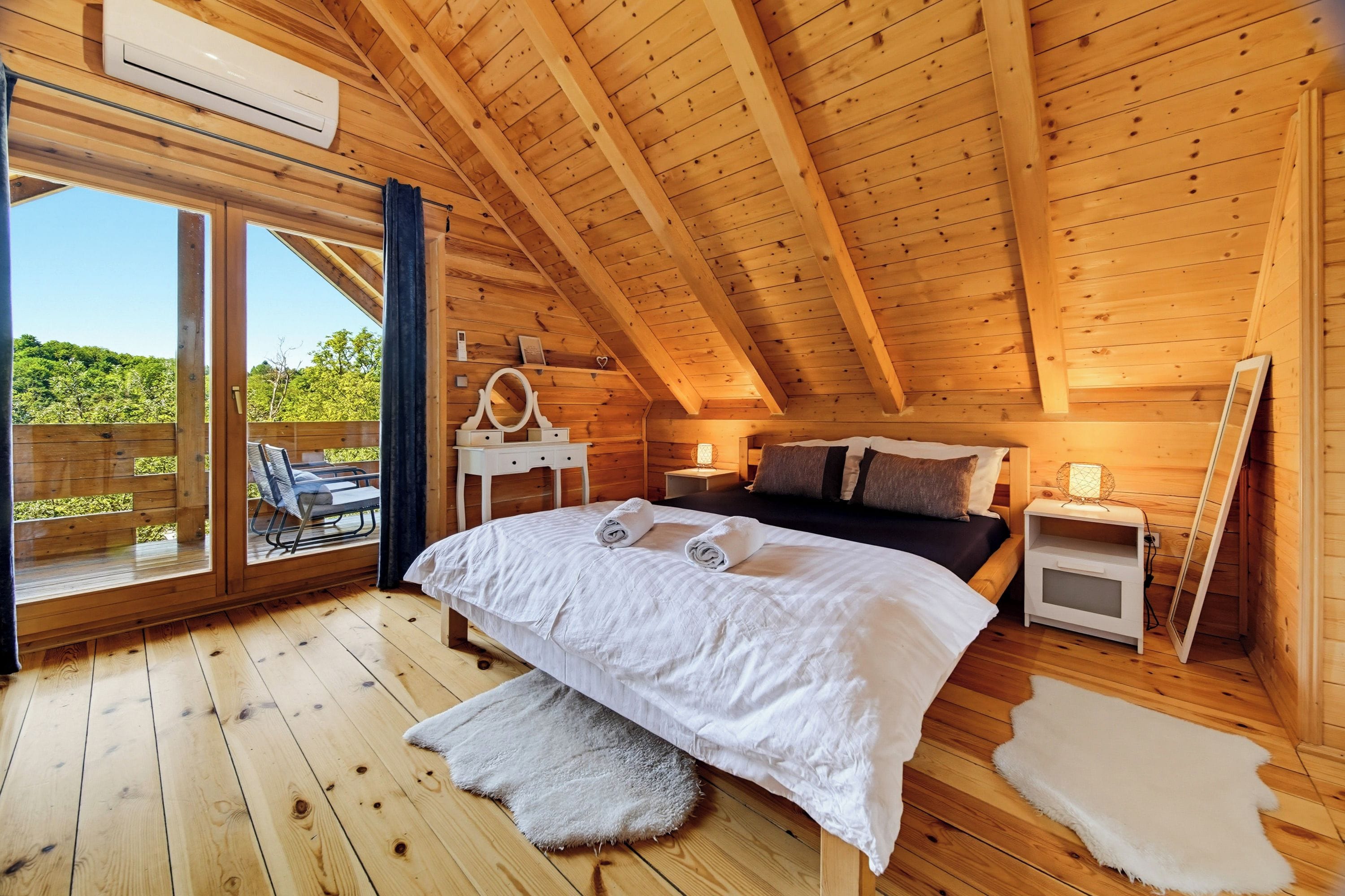 Un dormitorio tipo cabaña de madera con una cama, mesitas de noche y vistas por una puerta corrediza.