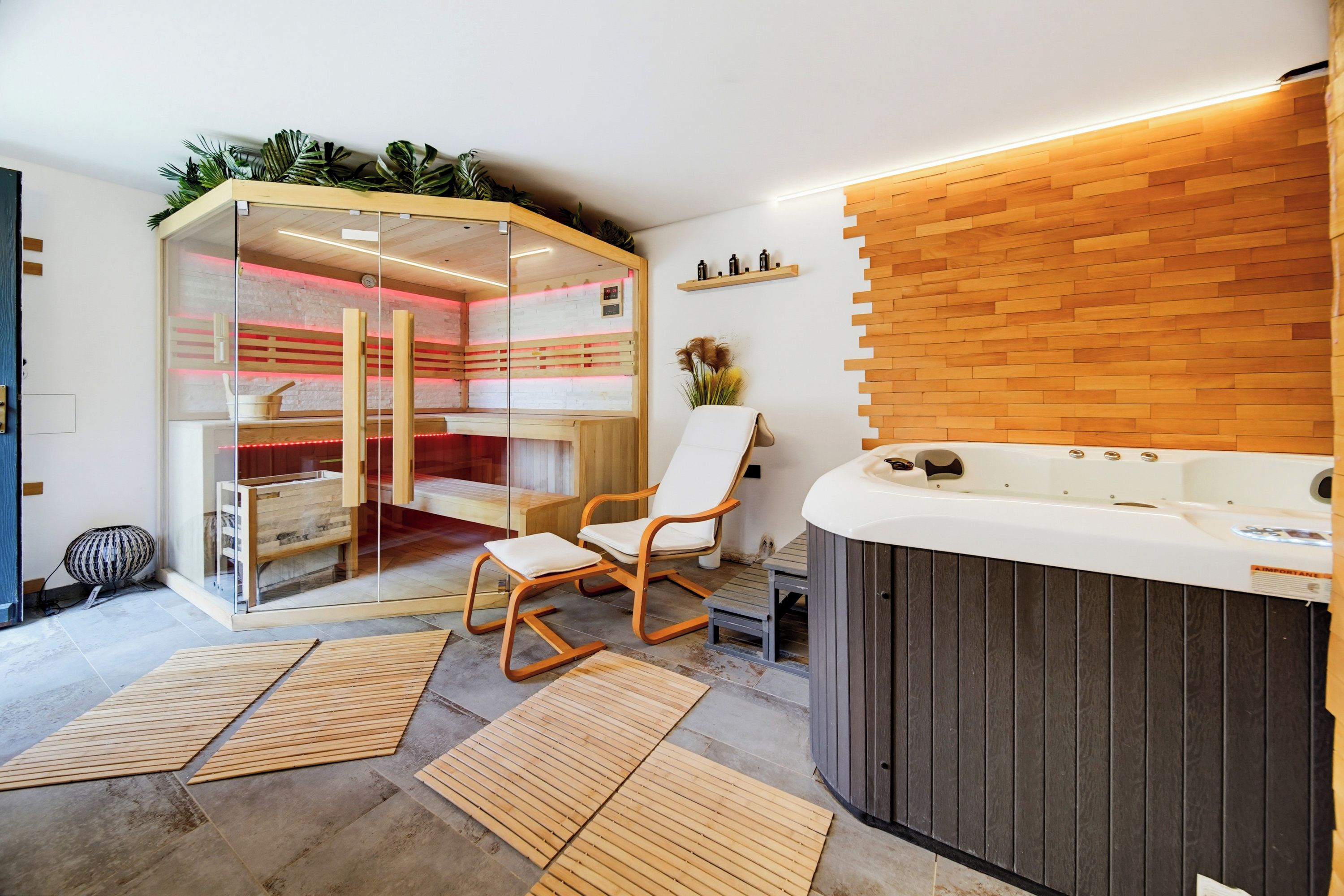 A spa room with a glass enclosure, wooden flooring, a hot tub, and a chair.