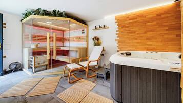 A spa room with a glass enclosure, wooden flooring, a hot tub, and a chair.