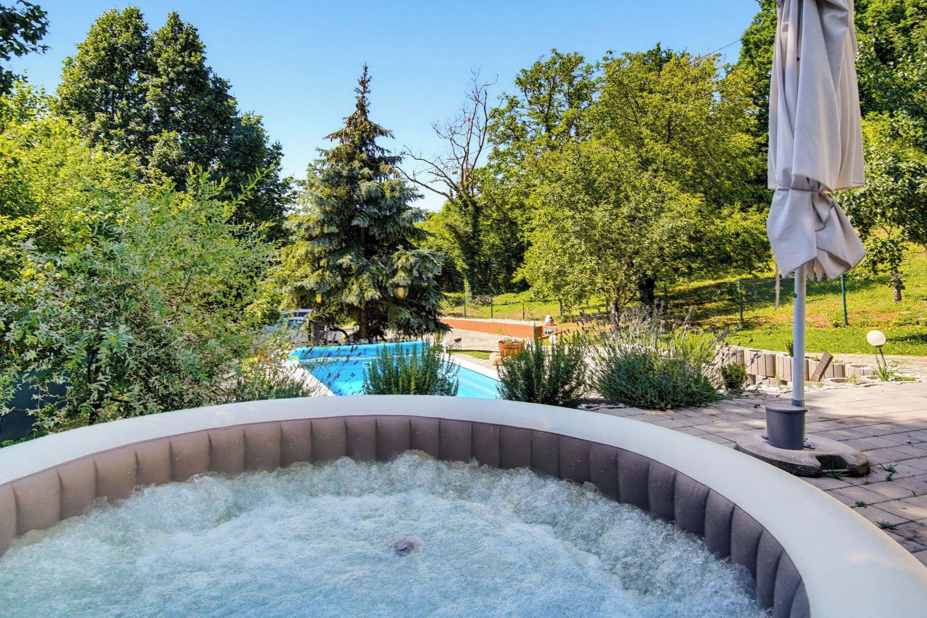 A hot tub surrounded by lush greenery and a swimming pool in the background.