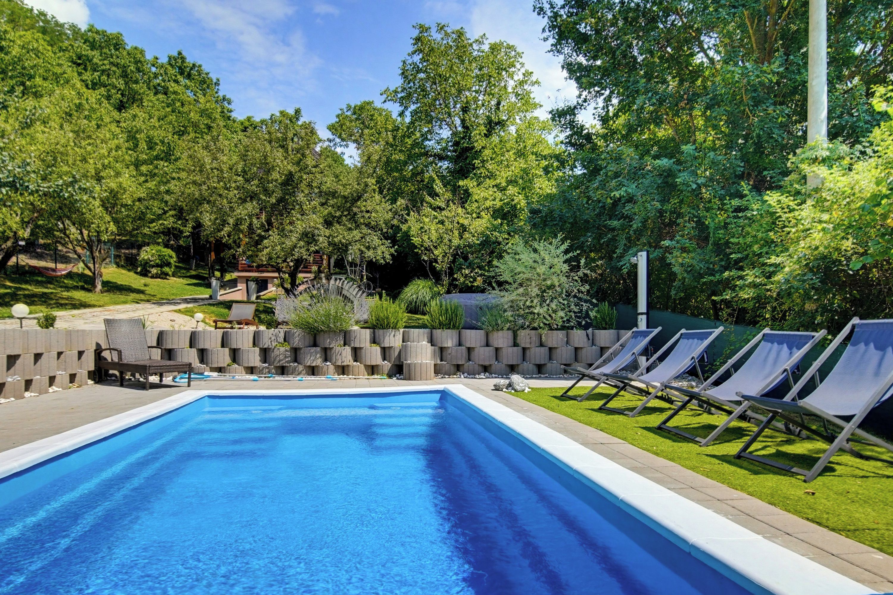 Una piscina rectangular con borde de azulejos, rodeada de césped y un bajo muro de piedra.