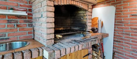 A brick oven with a wooden counter and a sink, a whiteboard, and a brick wall.