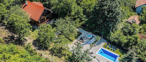 An aerial view of a property with a swimming pool, a red-roofed cabin, and surrounding greenery.