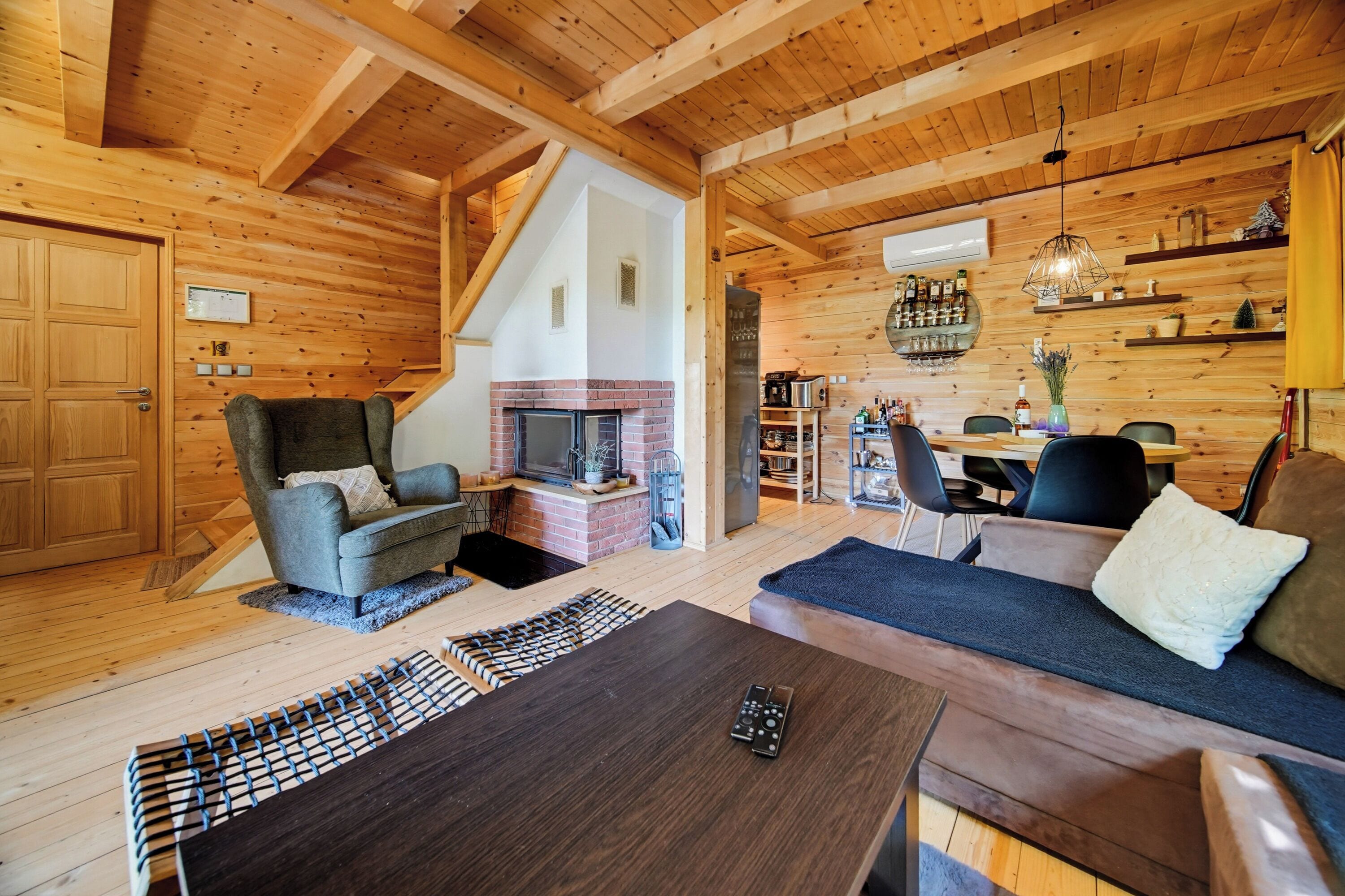 A cozy cabin interior with a fireplace, wooden walls, a dining area, and a sofa.
