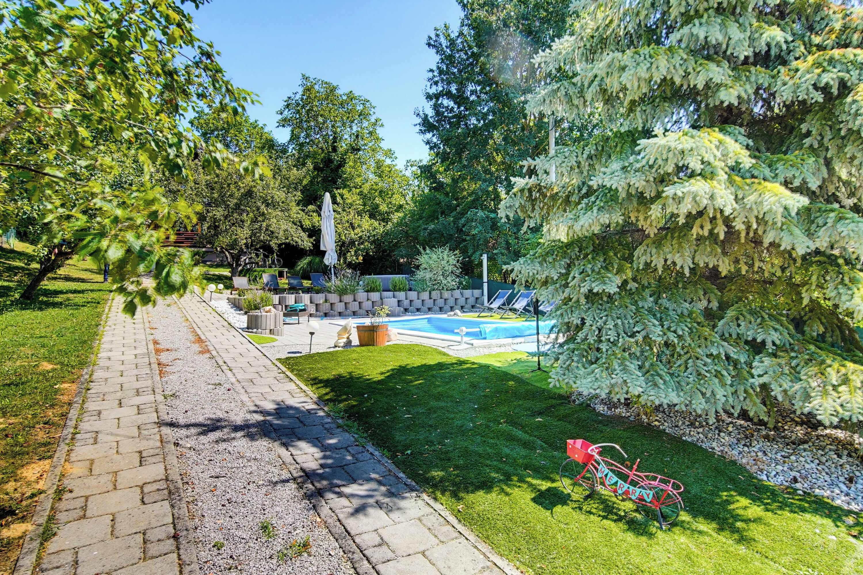 A backyard with a swimming pool, a paved pathway, and a bicycle.