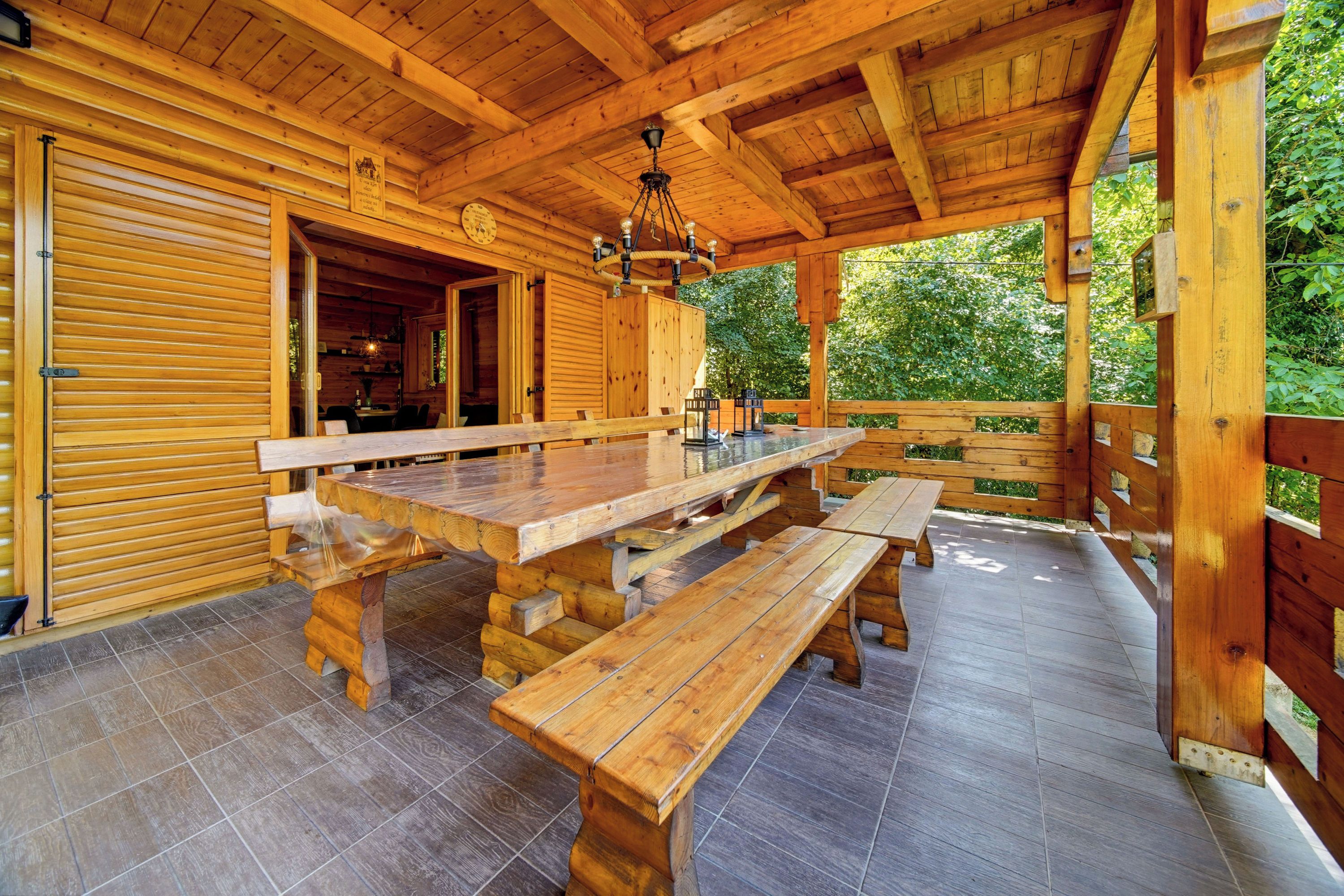 A wooden outdoor dining area with a large table and benches, surrounded by wooden walls and a covered roof.