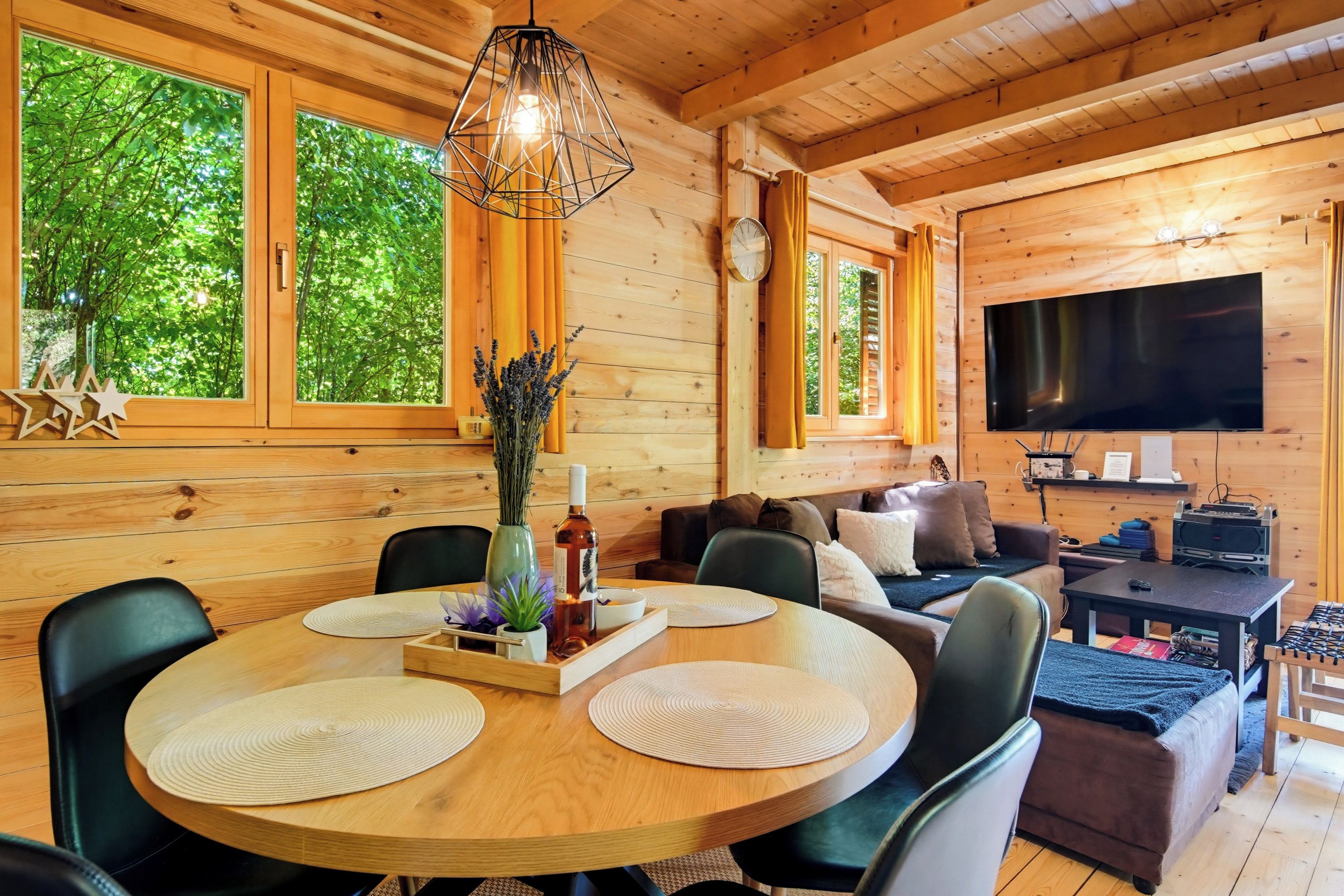 L’intérieur d’un chalet en bois comprend une table à manger, des chaises, un canapé, un téléviseur et de grandes fenêtres.