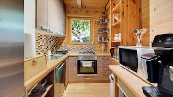A compact kitchen with wooden cabinets, a microwave, a coffee maker, and a window with a view of trees.
