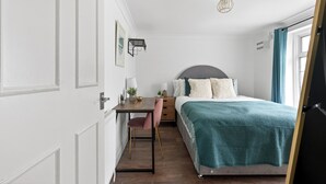 Ein Schlafzimmer mit einem Bett, einem Schreibtisch, einem Stuhl, einem Nachttisch, einer Lampe, einem Deckenventilator und einem Fenster mit Vorhängen.